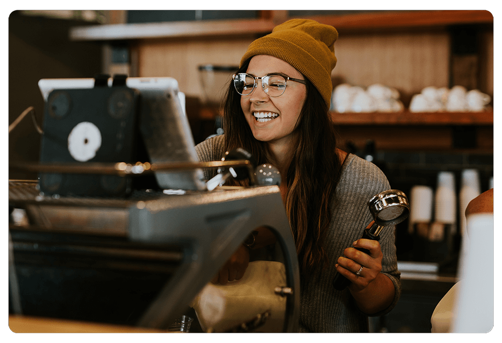 barista holding an espresso portafilter smiling at joe barista tablet sitting on top of the espresso machine