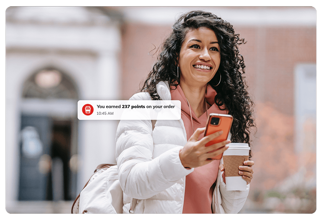 woman holding coffee to-go cup and iphone with a joe rewards notification that says 