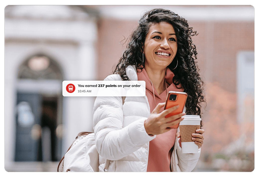 woman holding coffee to-go cup and iphone with a joe rewards notification that says "You earned 237 points on your order"