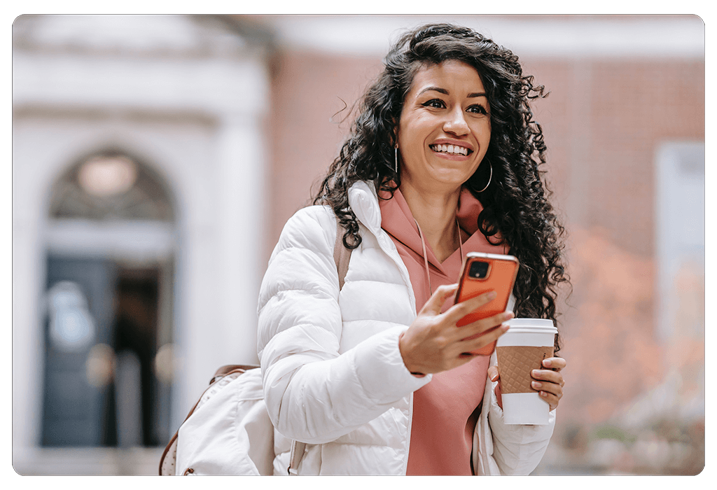woman smiling holding coffee cup to-go and iphone